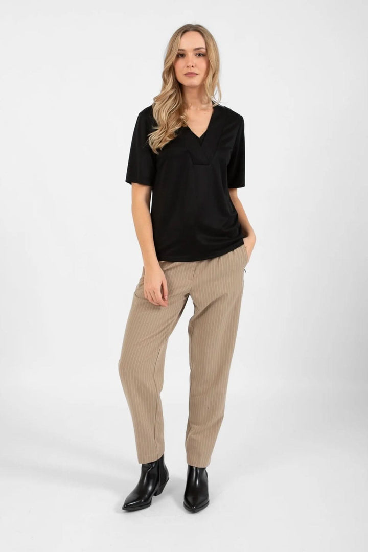 Femme portant un pantalon Stella beige à rayures et un haut noir, look chic et décontracté.