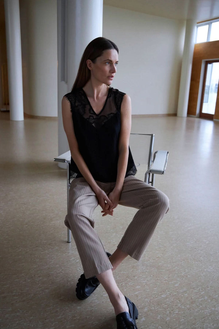 Femme portant un haut noir en dentelle et un pantalon Stella rayé, dans un espace moderne.