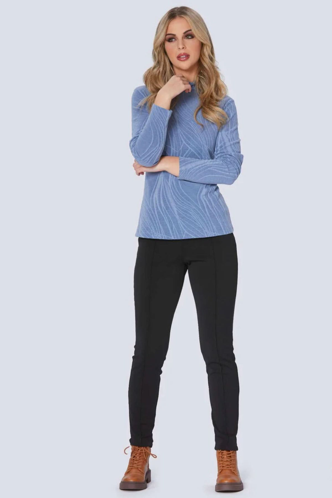 Femme en pantalon Tulio noir et haut bleu, look moderne et élégant, avec bottes marron.