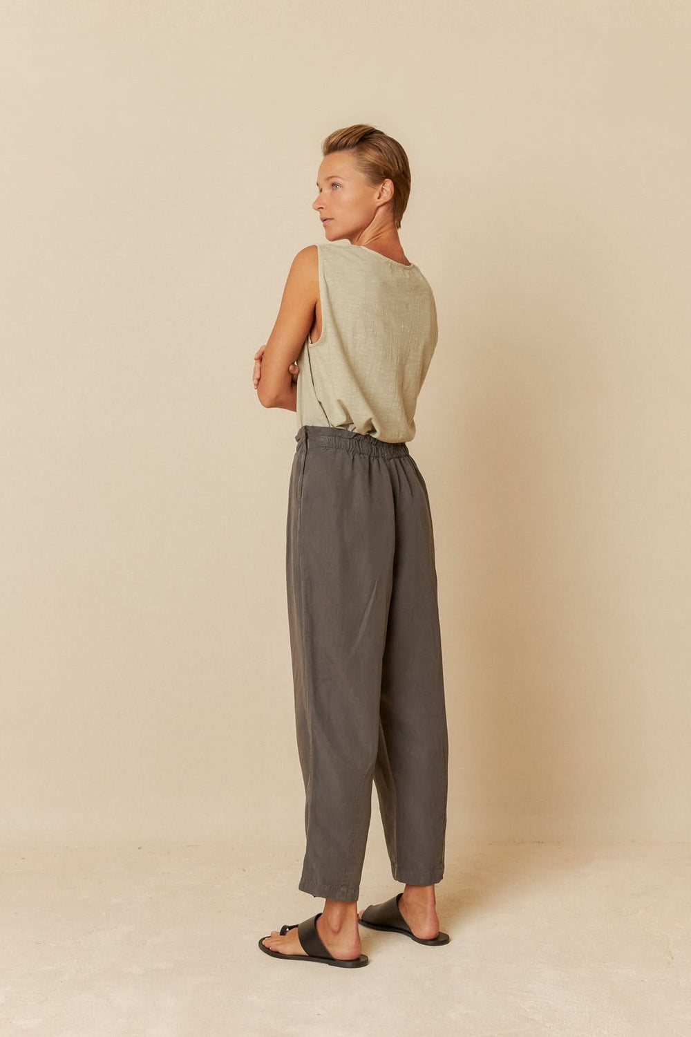 Femme portant un pantalon ample gris à taille élastiquée, vue de dos, sur fond neutre.