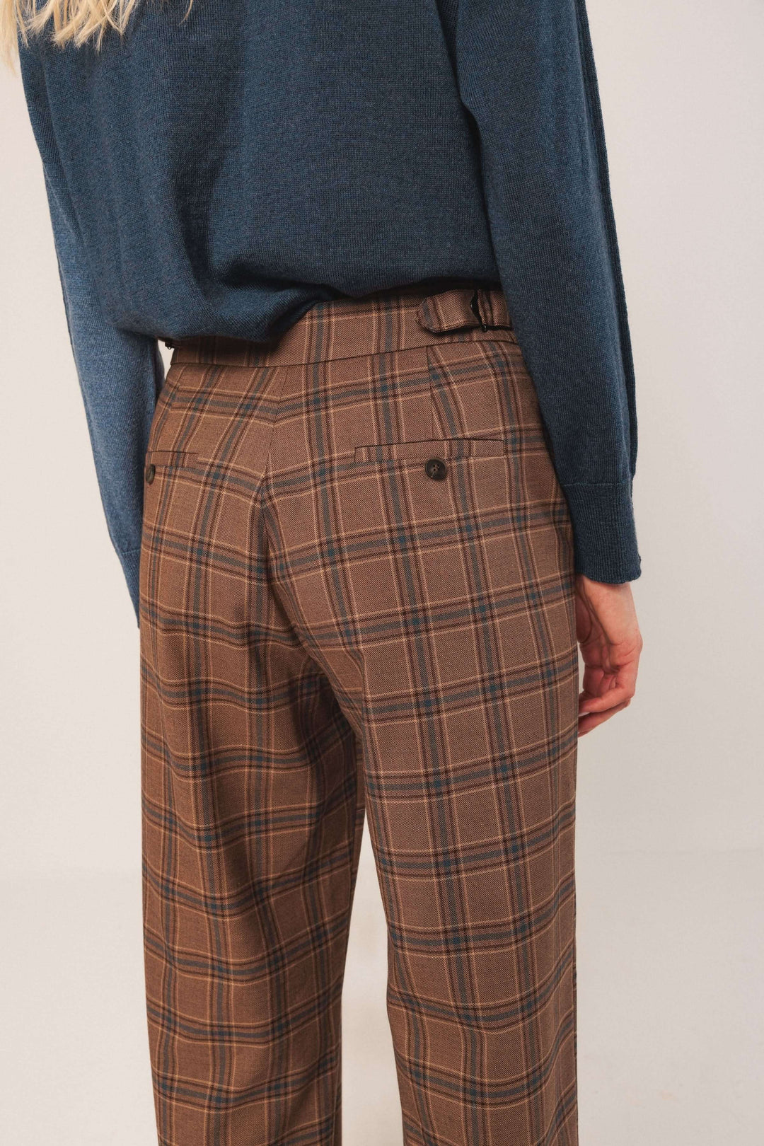 Pantalon à carreaux marron avec taille haute, coupe fluide et détails chics, porté avec un pull bleu.