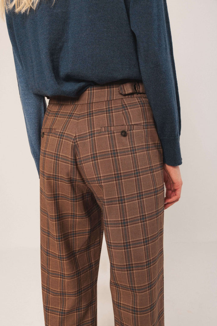 Pantalon à carreaux marron avec taille haute, coupe fluide et détails chics, porté avec un pull bleu.