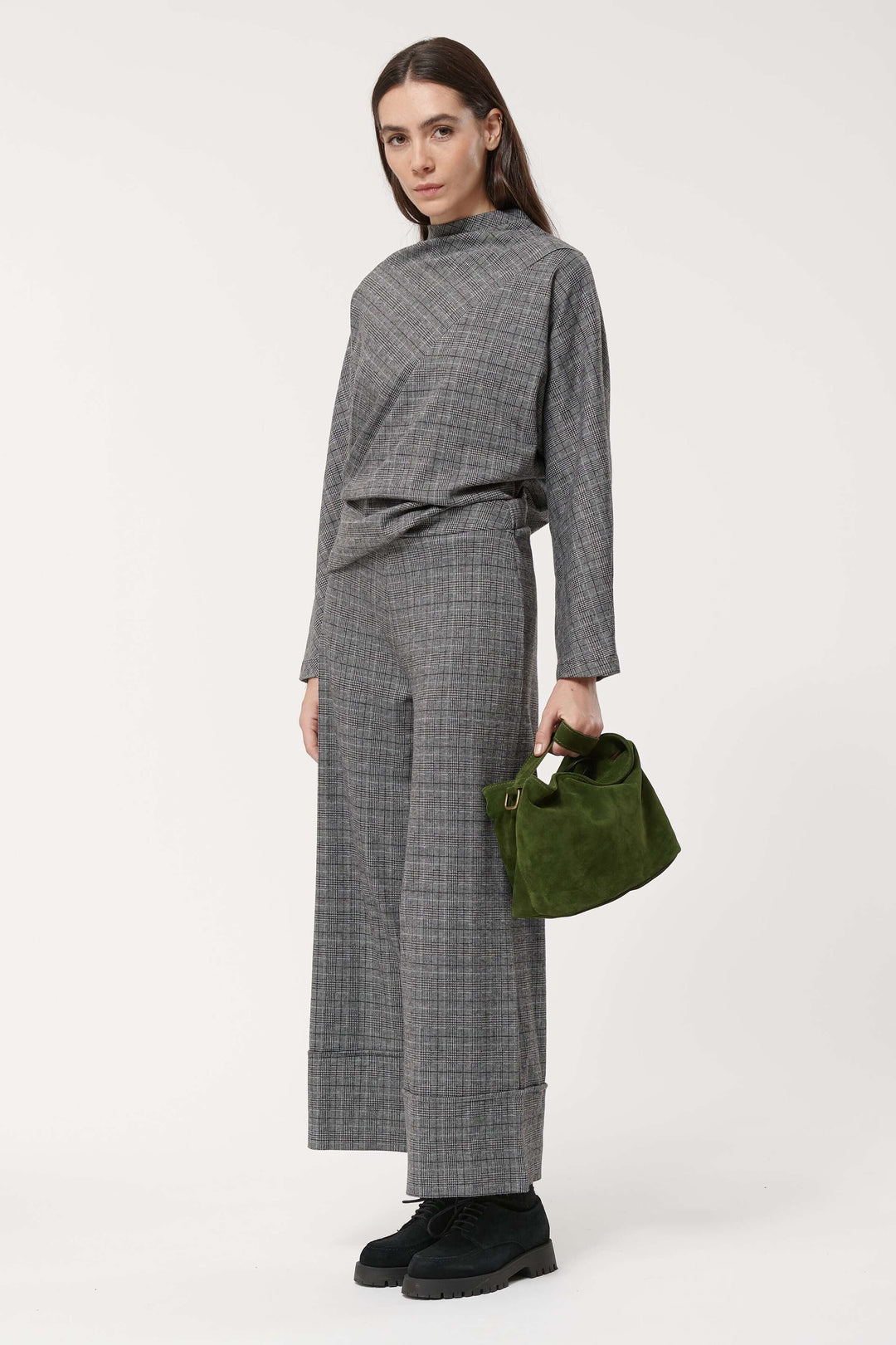 Femme en pantalon à carreaux large avec un haut gris et un sac vert, style élégant et moderne.