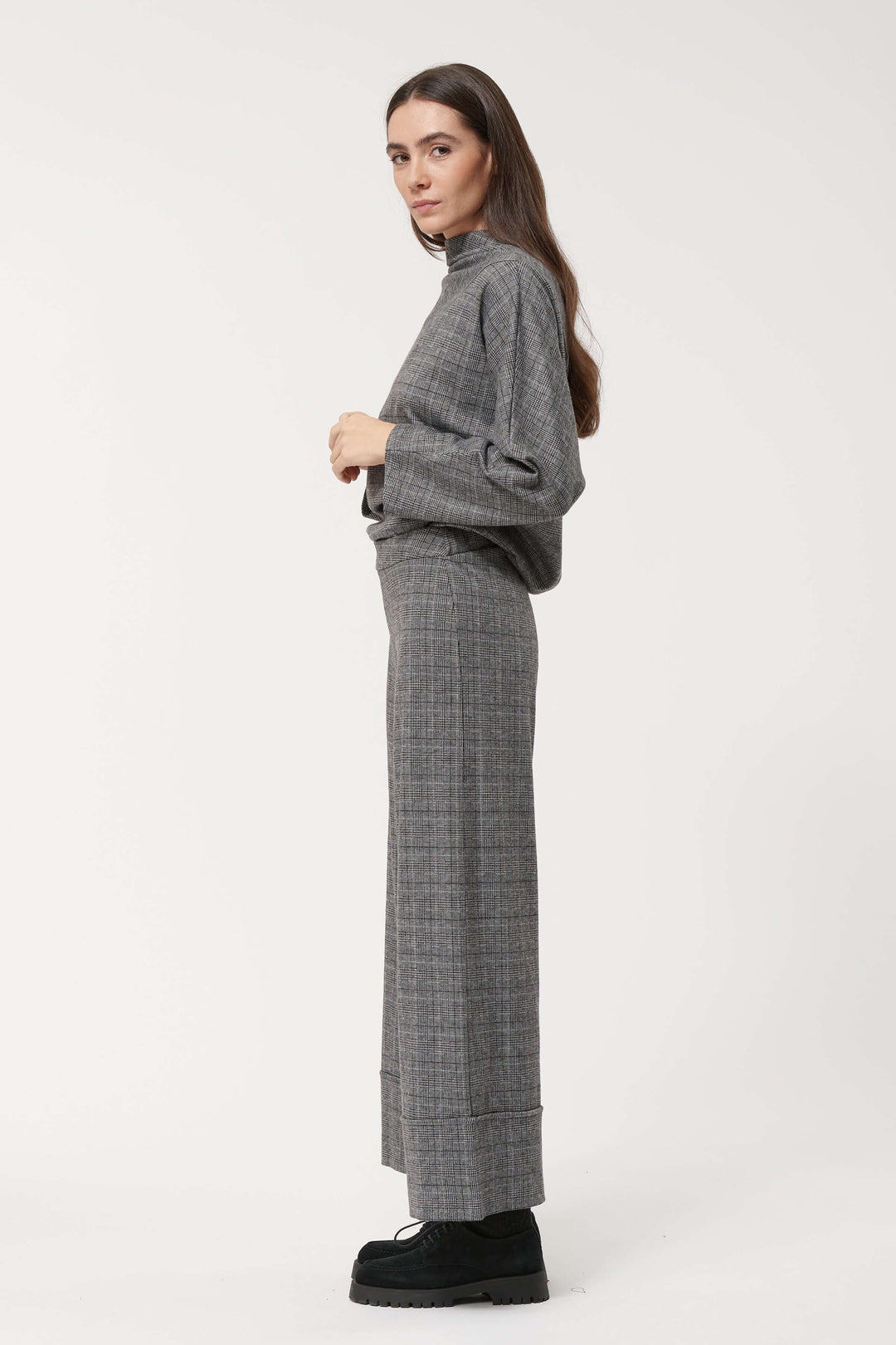 Pantalon à carreaux large et fluide avec taille haute, porté avec un pull gris, style chic et décontracté.
