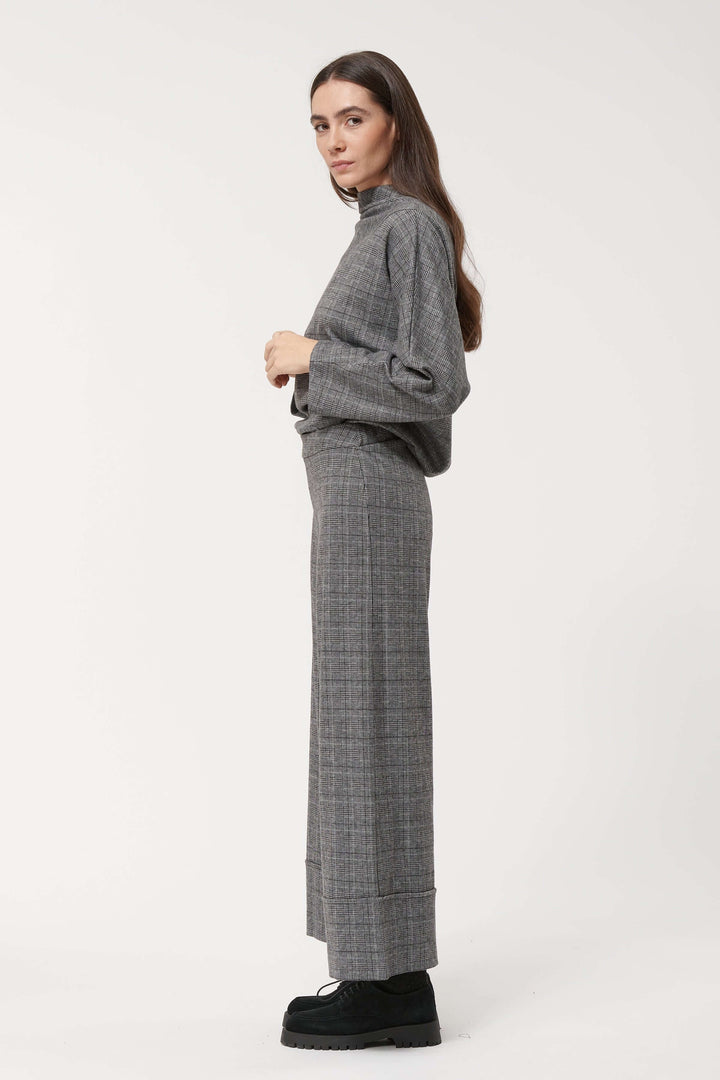 Pantalon à carreaux large et fluide avec taille haute, porté avec un pull gris, style chic et décontracté.