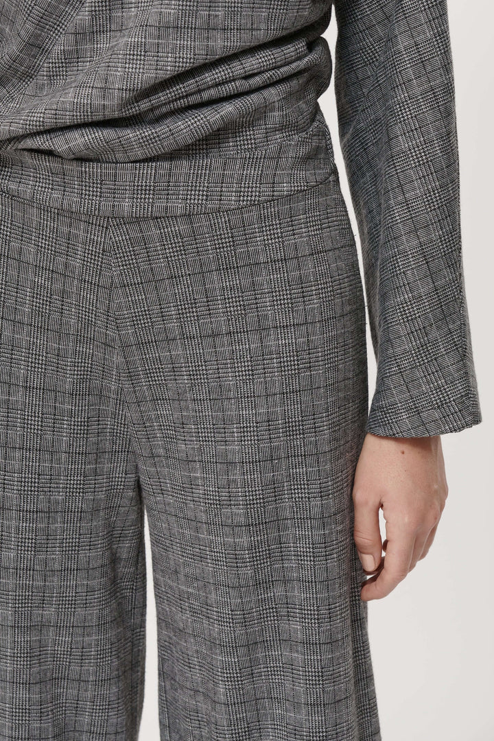 Détail d'un pantalon à carreaux gris à taille haute et coupe fluide, associé à un haut assorti.