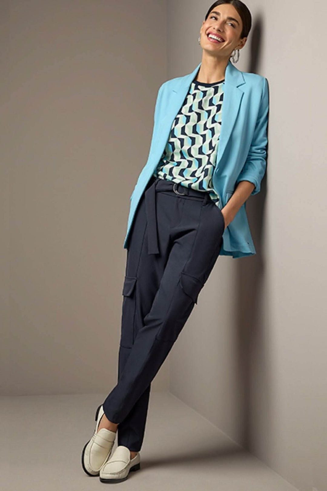 Femme souriante portant un ensemble chic avec un blazer bleu et un pantalon ceinturé jogger, complété par des chaussures blanches.