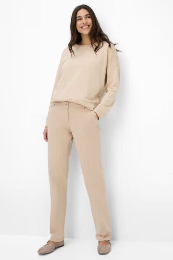 Femme souriante portant un pantalon chino Maron beige, associé à un haut décontracté et des chaussures confortables.