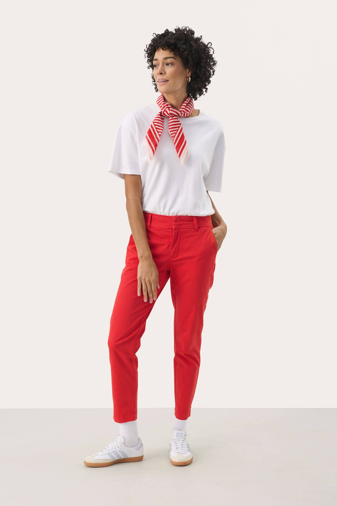 Femme portant un pantalon chino rouge et un t-shirt blanc avec un foulard rayé, idéale pour un look décontracté.