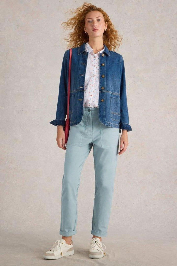 Femme en pantalon chino bleu clair avec chemise légère et veste en jean, style décontracté et élégant.