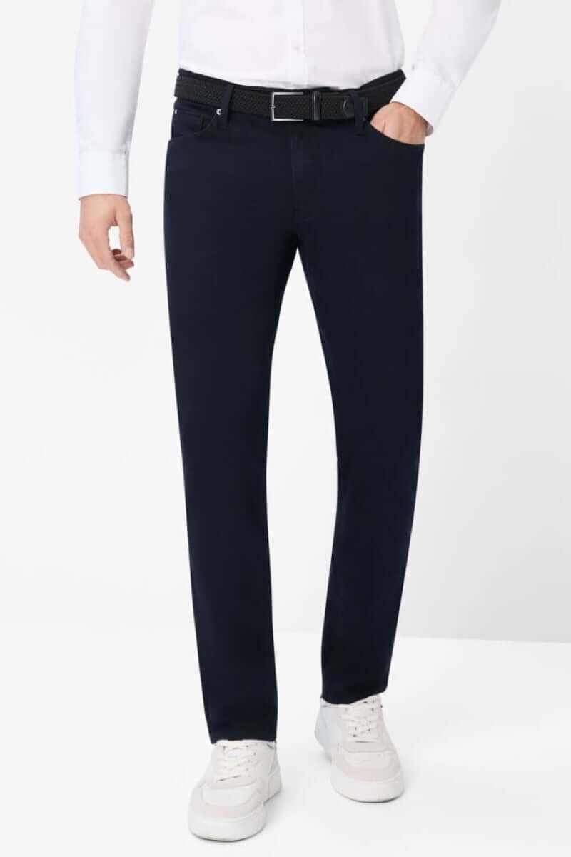 Pantalon à cinq poches moderne en tissu extensible, porté avec une chemise et des baskets blanches.