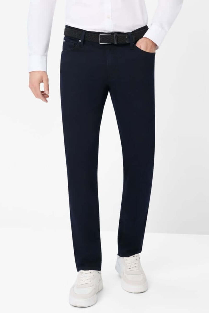 Pantalon à cinq poches moderne en tissu extensible, porté avec une chemise et des baskets blanches.