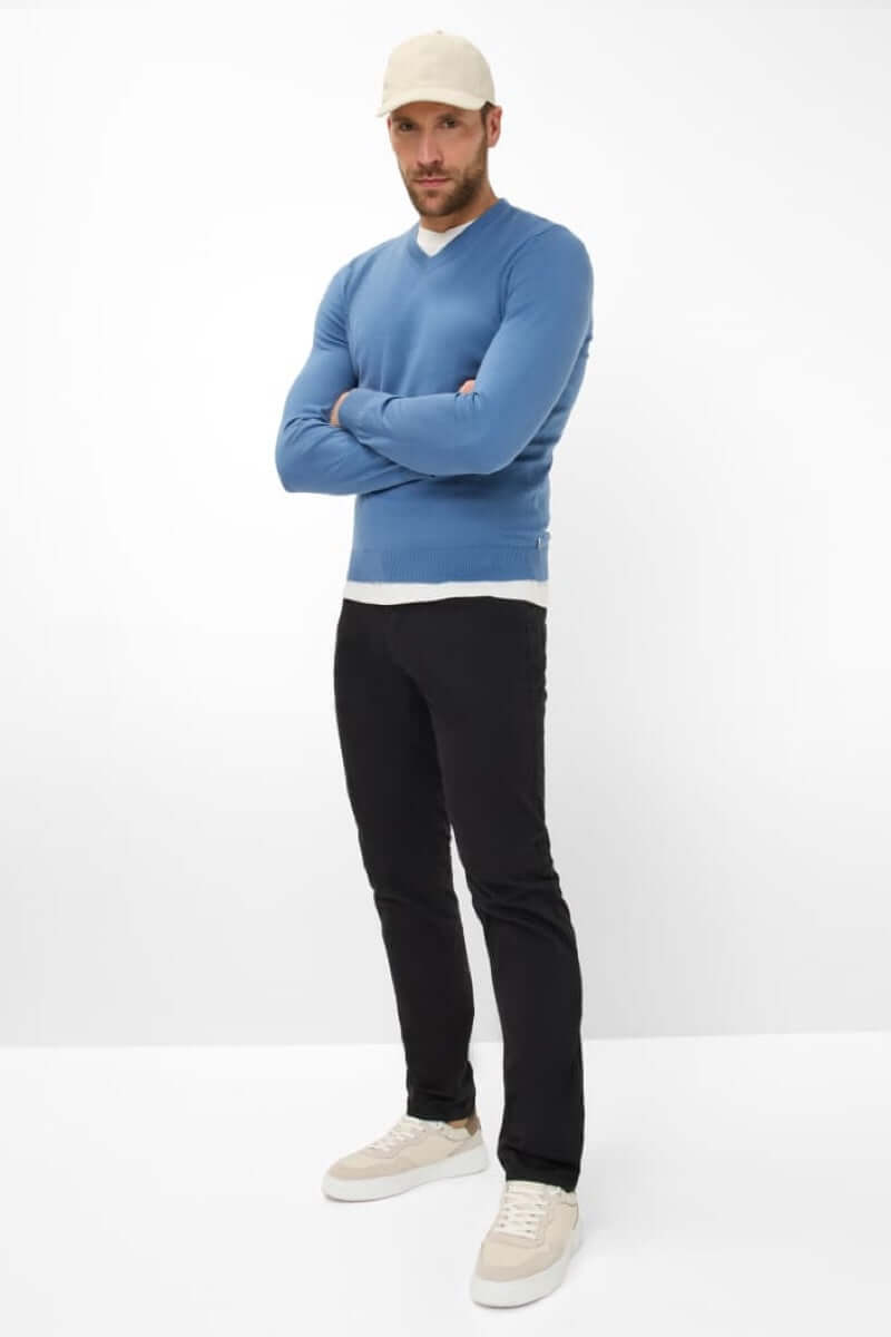 Homme portant un pull bleu et un pantalon noir, stylé casual avec sneakers beige.