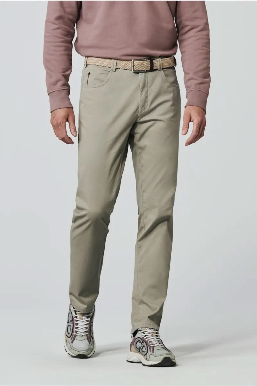 Pantalon décontracté beige avec coupe ajustée, porté avec un pull rose et des chaussures de sport.