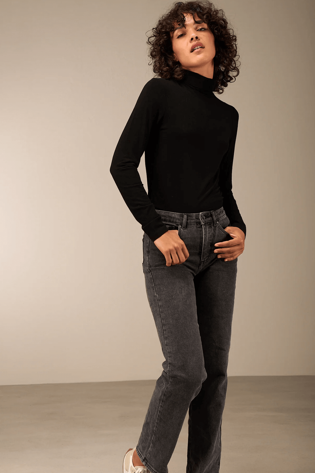 Femme portant un pantalon droit gris avec un chandail noir, illustrant un look moderne et polyvalent. Description du produit en français.
