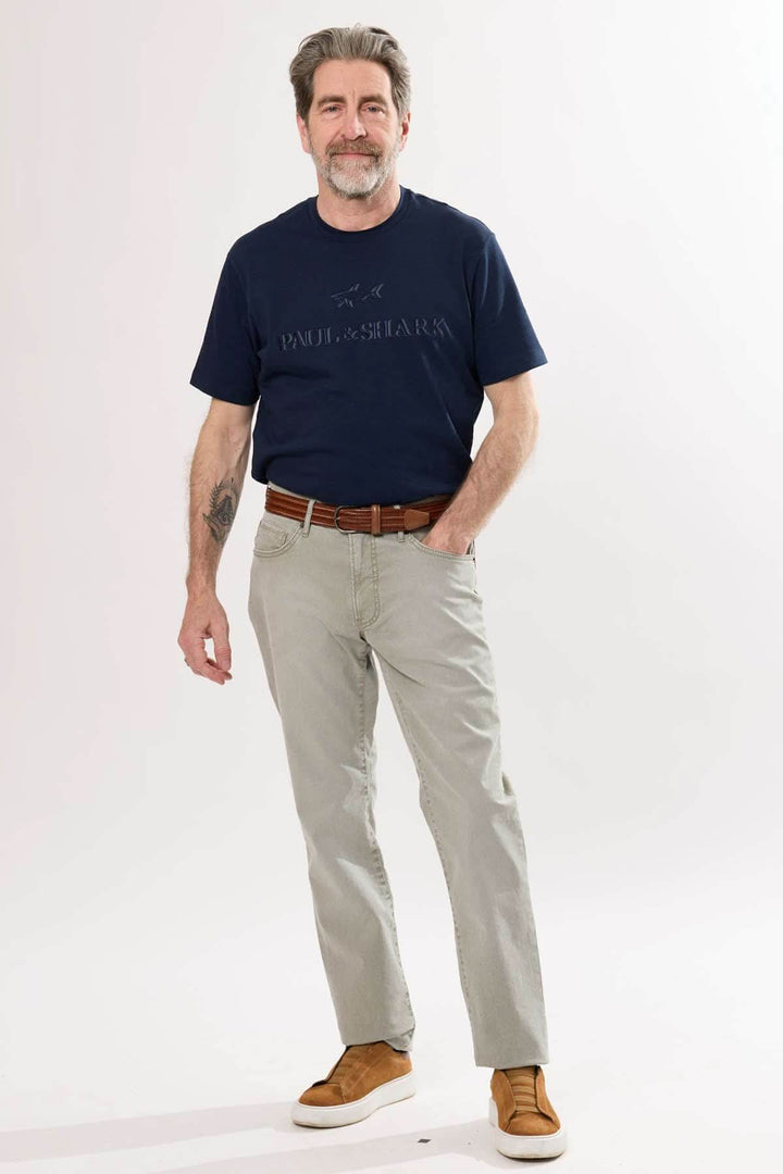 Homme portant un pantalon droit beige et un t-shirt bleu marine, style décontracté avec ceinture en cuir.