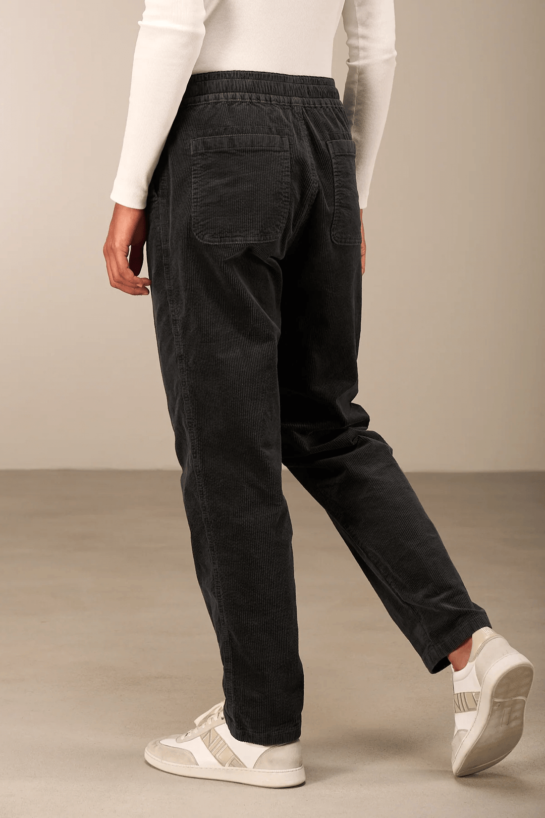 Pantalon en velours côtelé noir avec taille élastique et jambe fuselée, porté avec des baskets blanches, vue arrière.