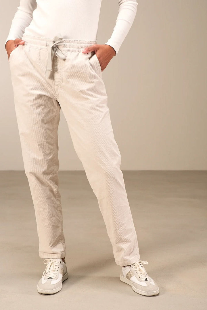 Pantalon beige en velours côtelé avec taille élastique et cordon, jambe fuselée. Look décontracté avec baskets blanches.