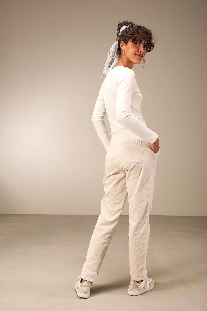Woman wearing white casual outfit with hands in pockets, standing on beige background, showcasing comfortable style.