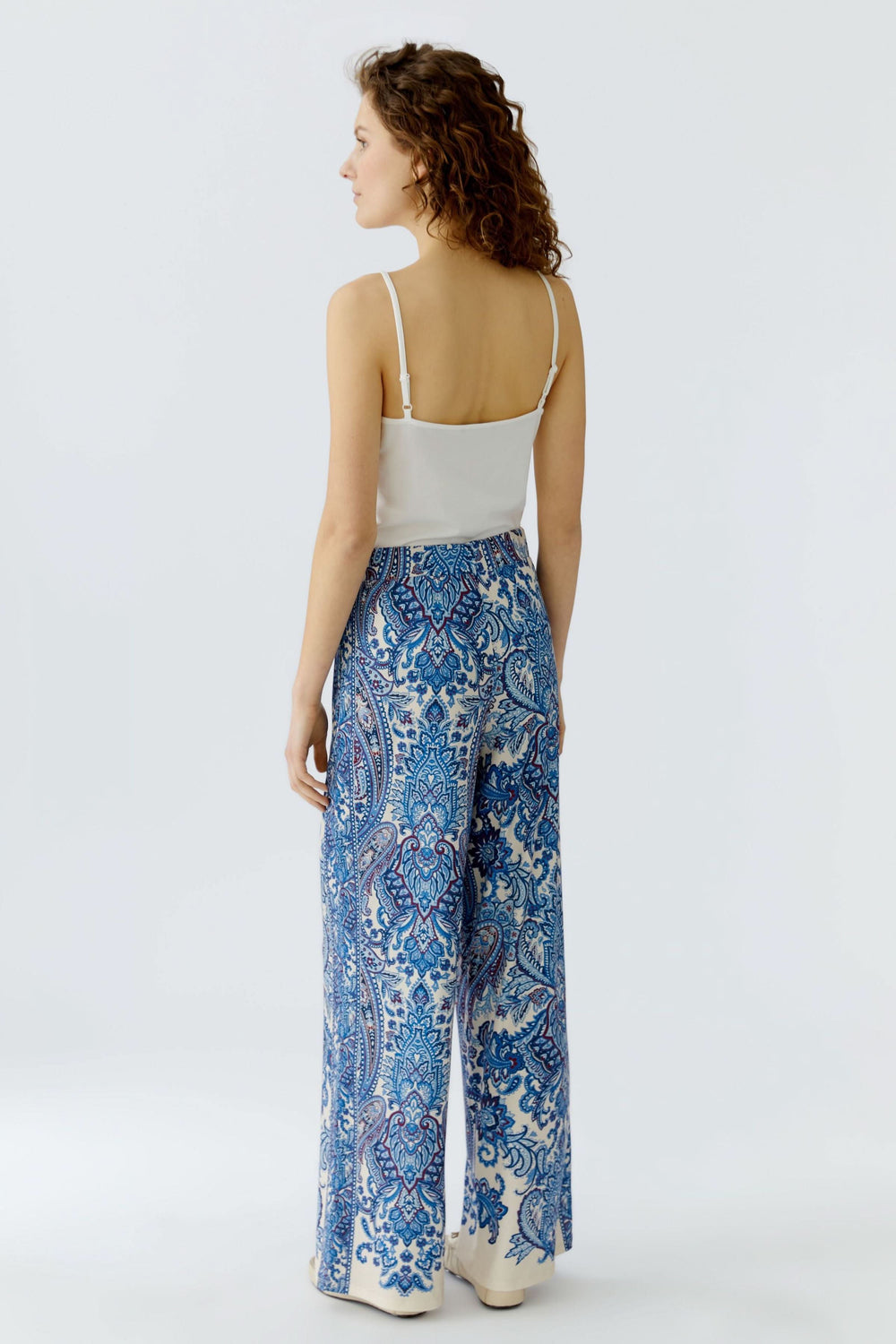 Femme portant un pantalon fluide à imprimé cachemire bleu, élégant et confortable, vue de dos.