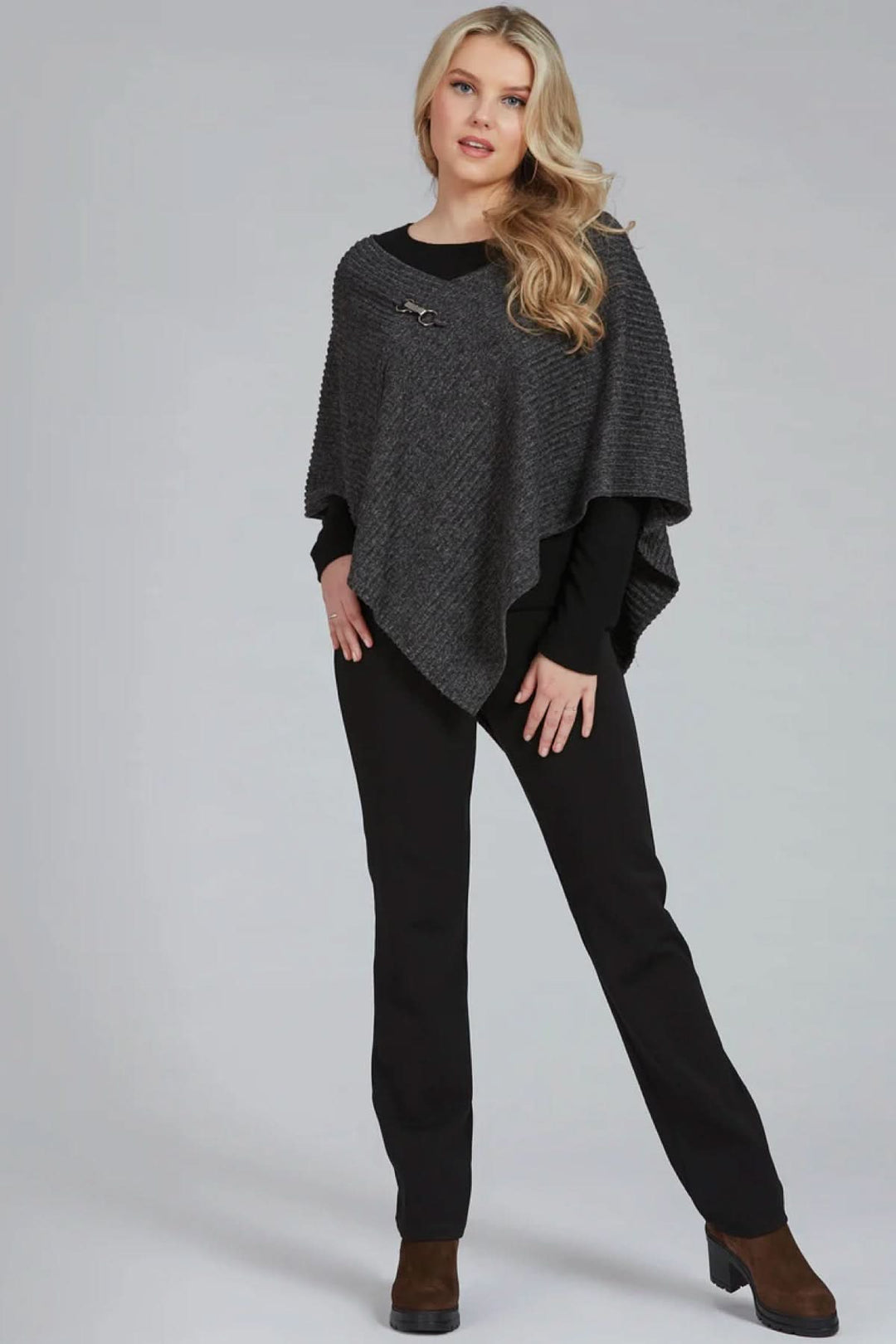 Femme portant un poncho gris et un pantalon noir, look chic et décontracté avec bottes.