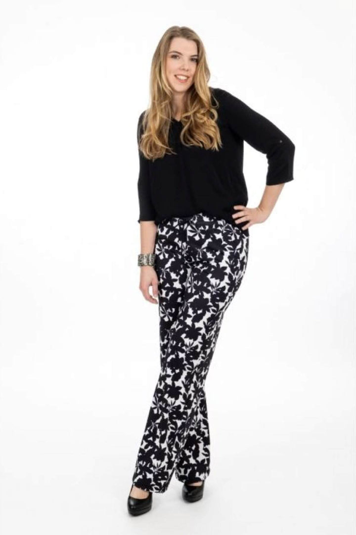 Femme souriante portant un pantalon à imprimé floral noir et blanc avec un haut noir, parfait pour un look estival élégant.