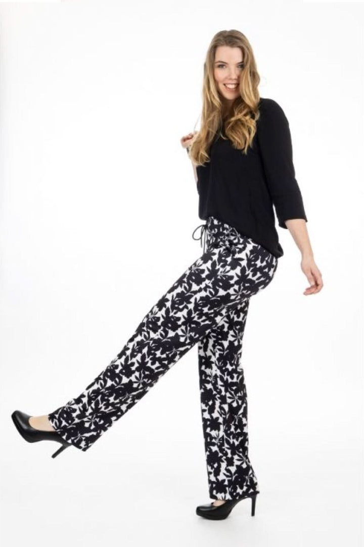 Femme souriante en pantalon fluide à imprimé floral noir et blanc, associé à un top noir.