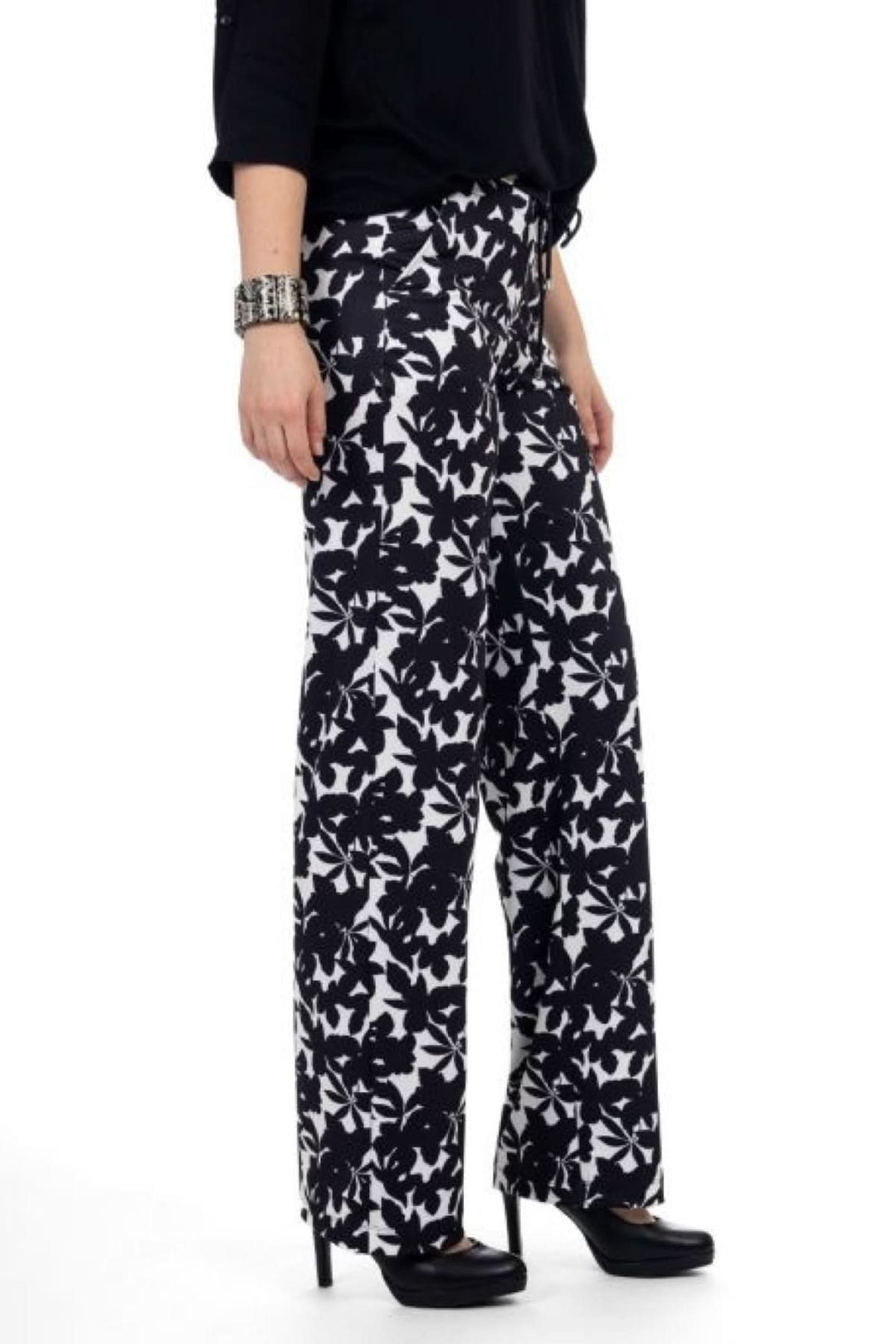 Pantalon à imprimé floral noir et blanc avec coupe fluide, porté avec un haut noir et des talons, style estival sophistiqué.