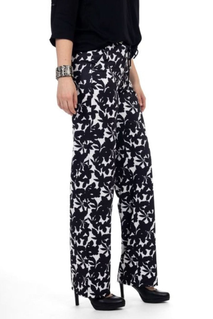 Pantalon à imprimé floral noir et blanc avec coupe fluide, porté avec un haut noir et des talons, style estival sophistiqué.