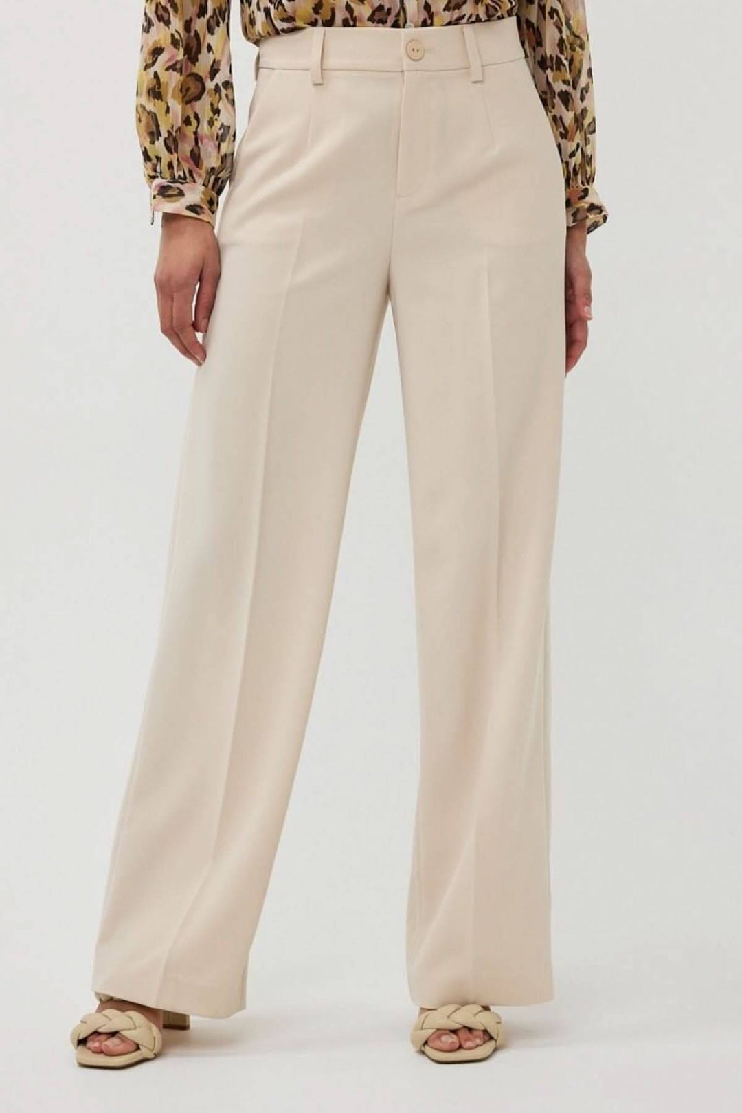 Pantalon à jambe large beige avec taille haute et plis marqués, porté avec une blouse imprimée.