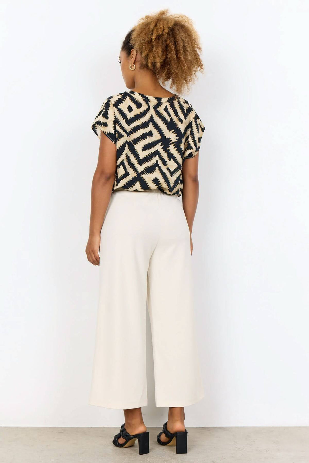 Femme portant un pantalon jambe large beige avec un haut à motif, vue arrière, style décontracté et confortable.