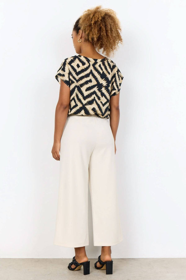 Femme portant un pantalon jambe large beige avec un haut à motif, vue arrière, style décontracté et confortable.