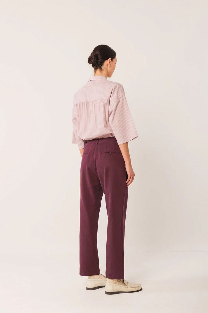 Personne portant un pantalon à la coupe droite bordeaux, de dos, associé à une chemise rose et des chaussures beige.