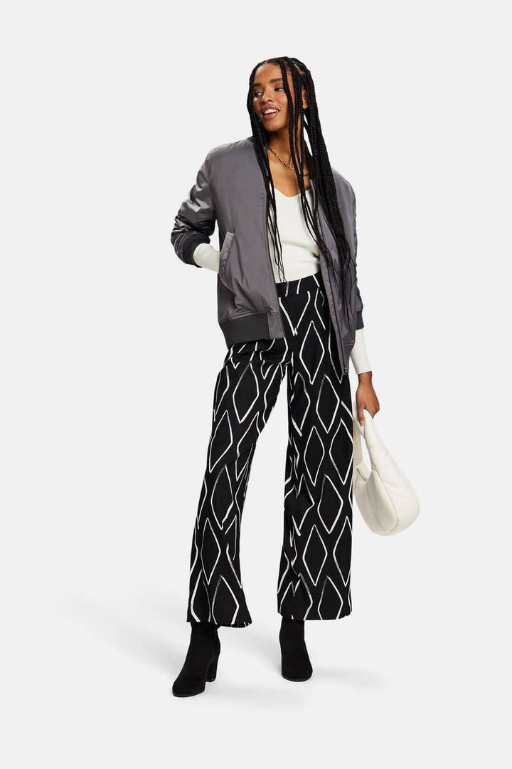 Femme portant un pantalon large à losanges noirs et blancs avec un bomber gris et une blouse blanche.