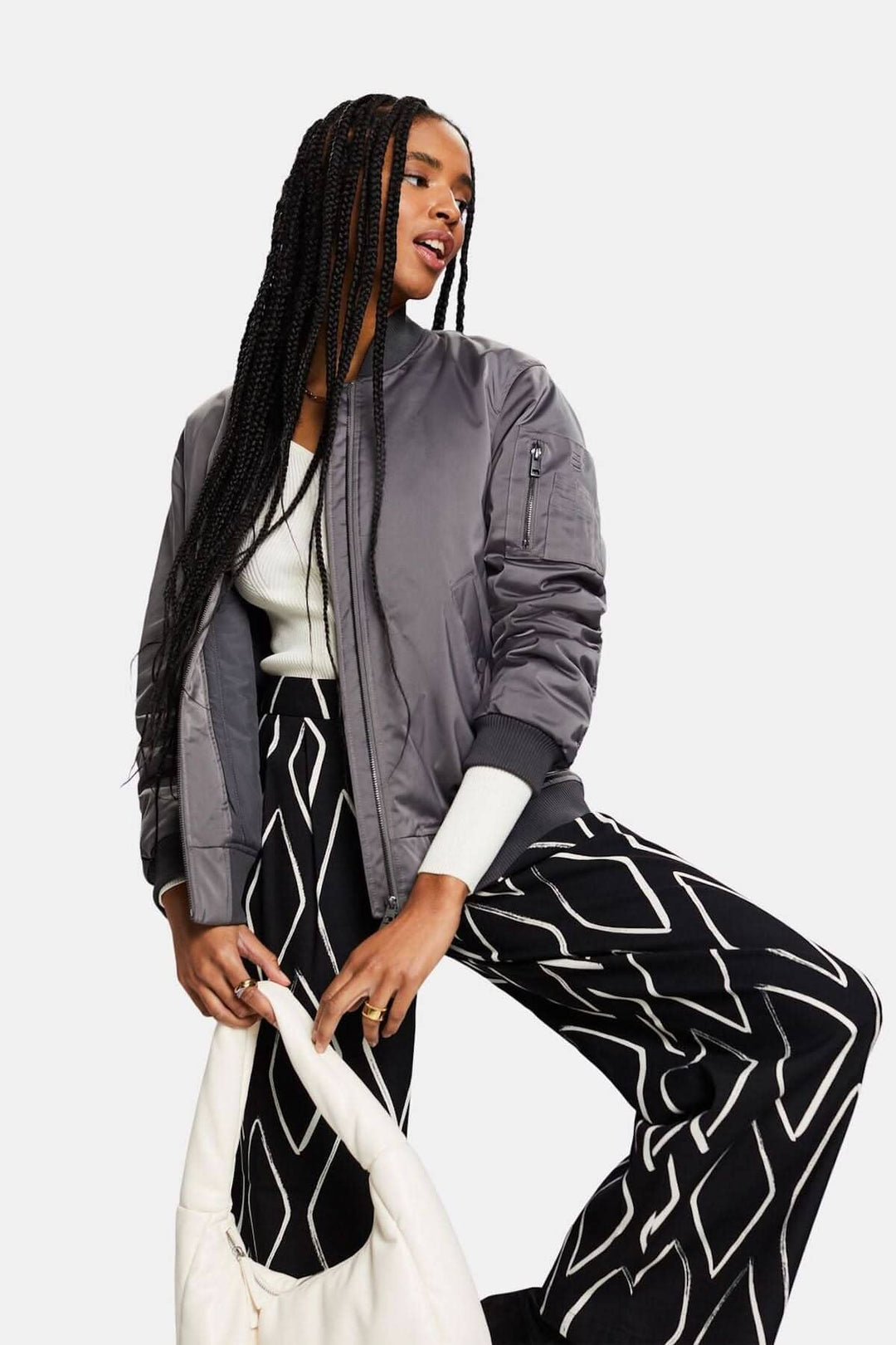 Femme portant un bomber gris avec pantalon large à motifs losanges et sac à main, pose décontractée.