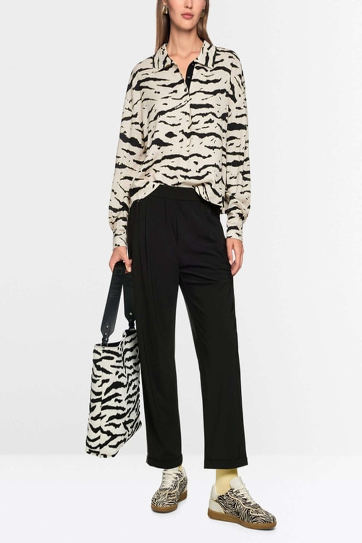 Femme portant le Pantalon léger WUXI noir avec chemise imprimée, sac assorti, et chaussures de sport élégantes.