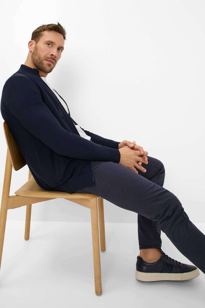 Homme assis sur une chaise, portant un pantalon marathon et un pull bleu marine, style décontracté et moderne.
