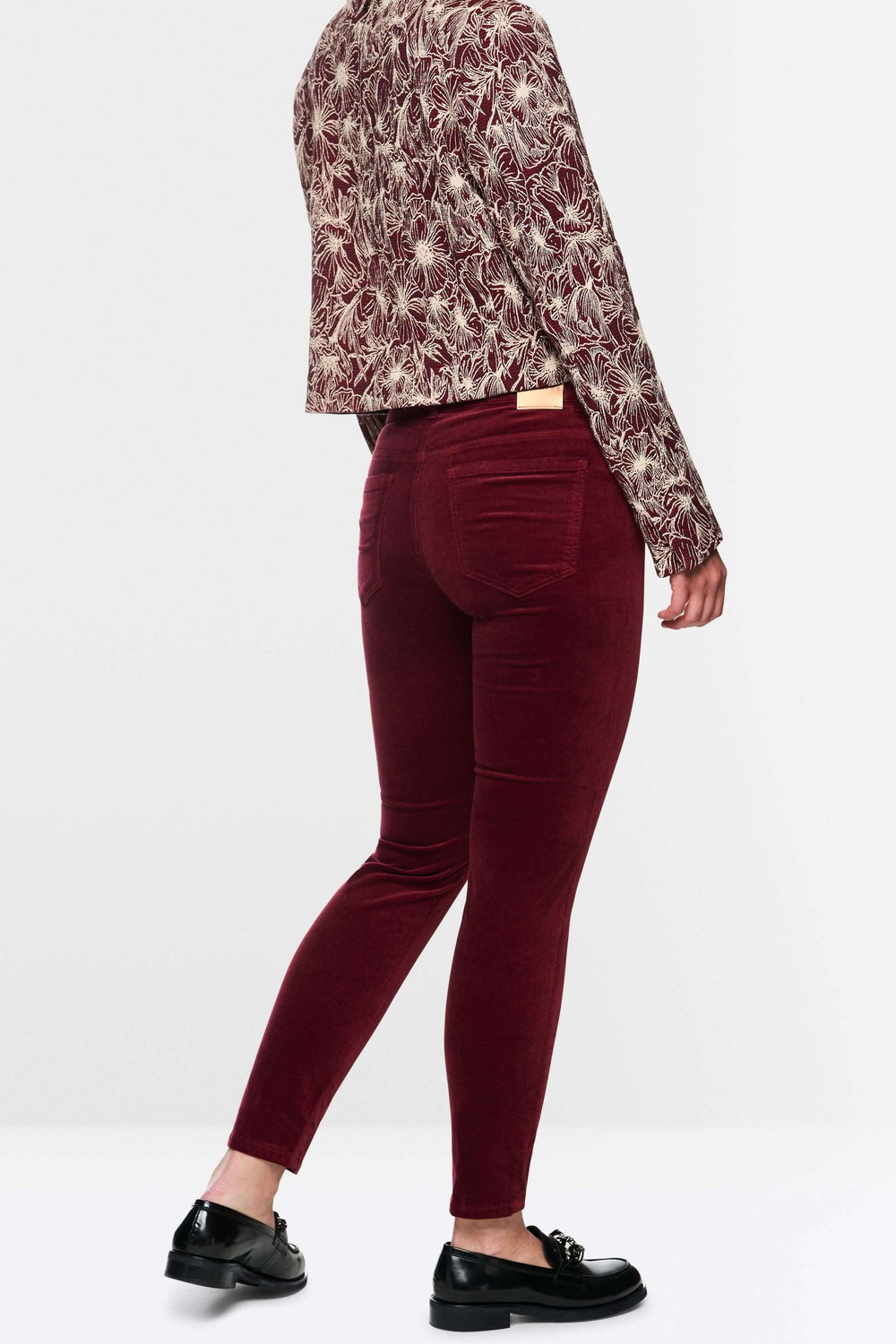 Pantalon taille basse en velours bordeaux avec coupe ajustée, porté avec une veste imprimée pour un look élégant et moderne.