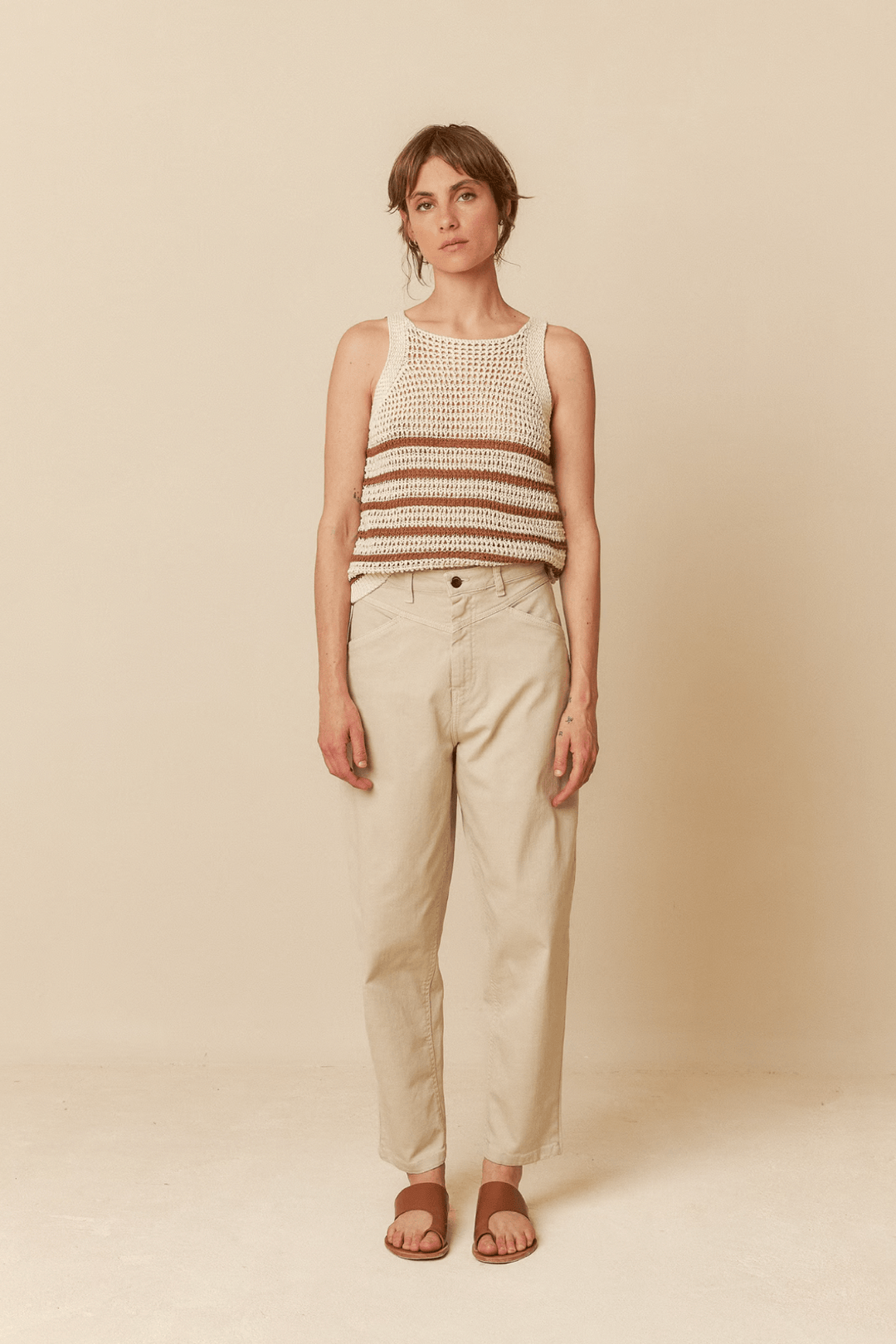 Femme portant un haut en tricot rayé et un pantalon beige, style décontracté et moderne.