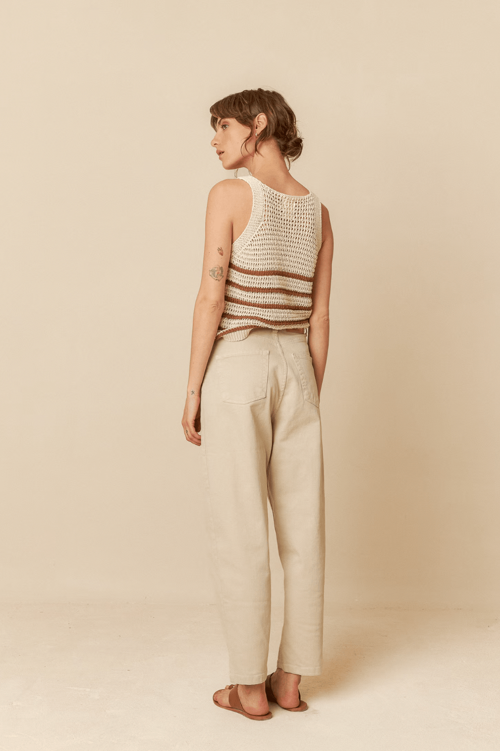 Femme vue de dos portant un pantalon taille haute beige et un top rayé en crochet.