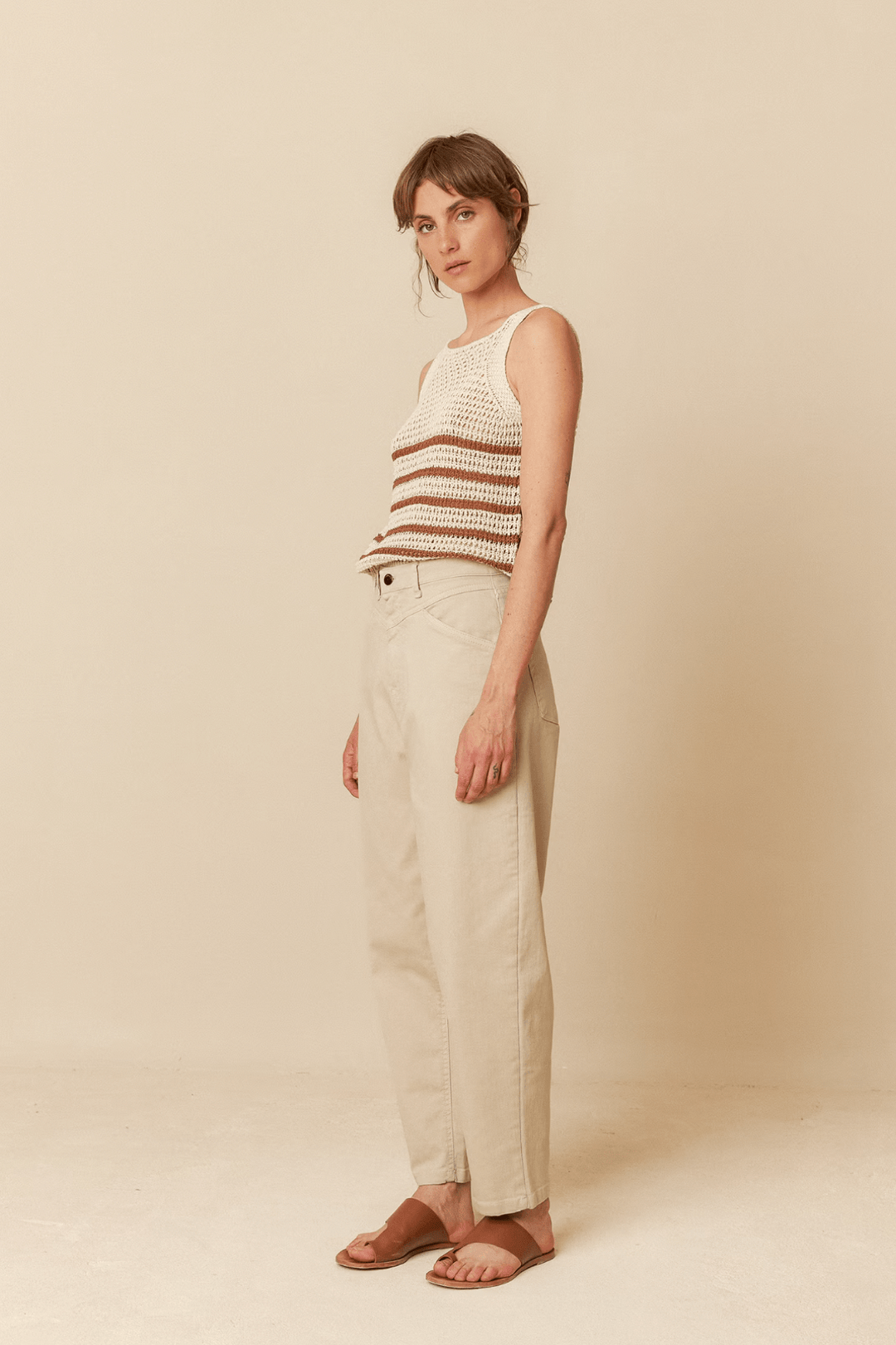 Pantalon taille haute beige avec empiècements, porté par une femme au top rayé, pour un look chic et moderne.