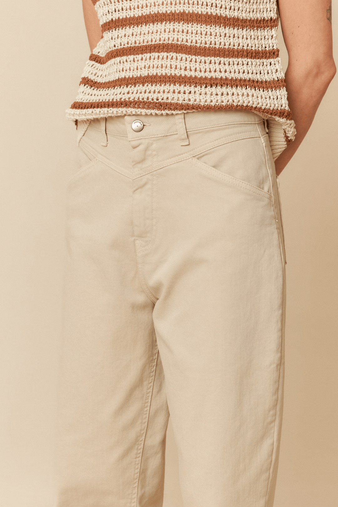Pantalon taille haute beige avec empiècements, porté avec un haut en tricot rayé, offrant une coupe moderne.