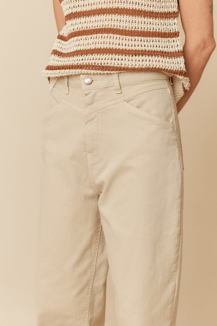 Pantalon taille haute beige avec empiècements, porté avec un haut en tricot rayé, offrant une coupe moderne.