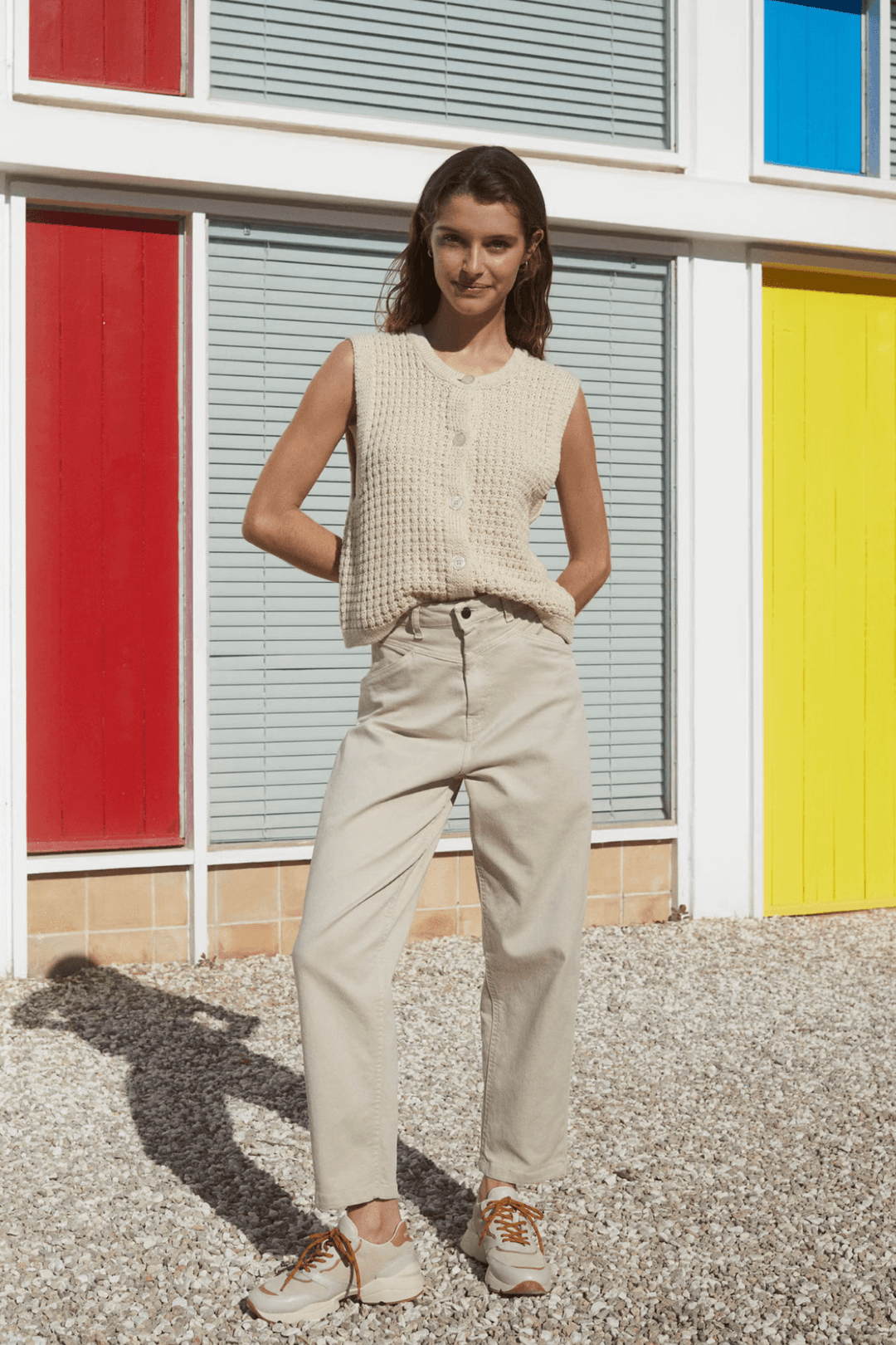Modèle féminine portant un pantalon taille haute beige avec un haut sans manches dans un décor coloré.