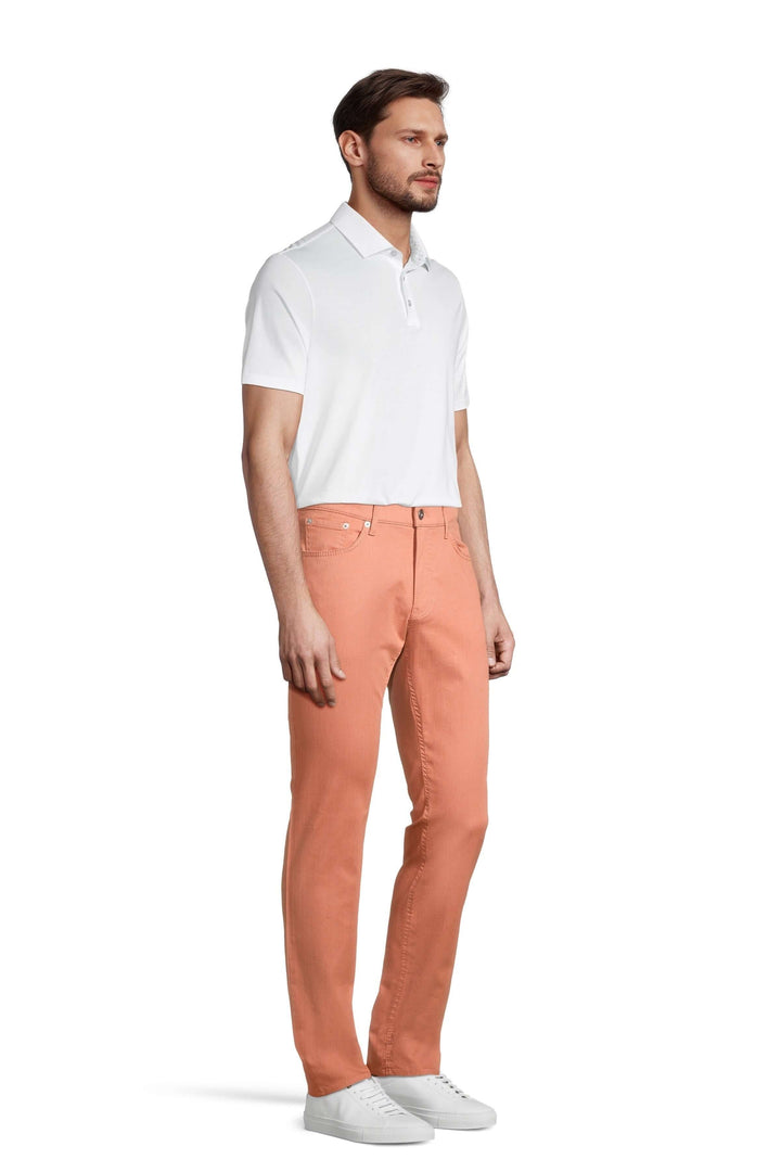 Homme portant un pantalon à taille élastique en couleur pêche, associé à un polo blanc, avec des baskets blanches.
