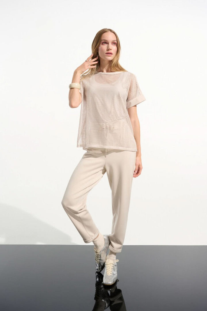 Femme portant Pantalon à taille nouée coupe droite beige avec un haut en tissu transparent et des baskets blanches sur fond blanc.