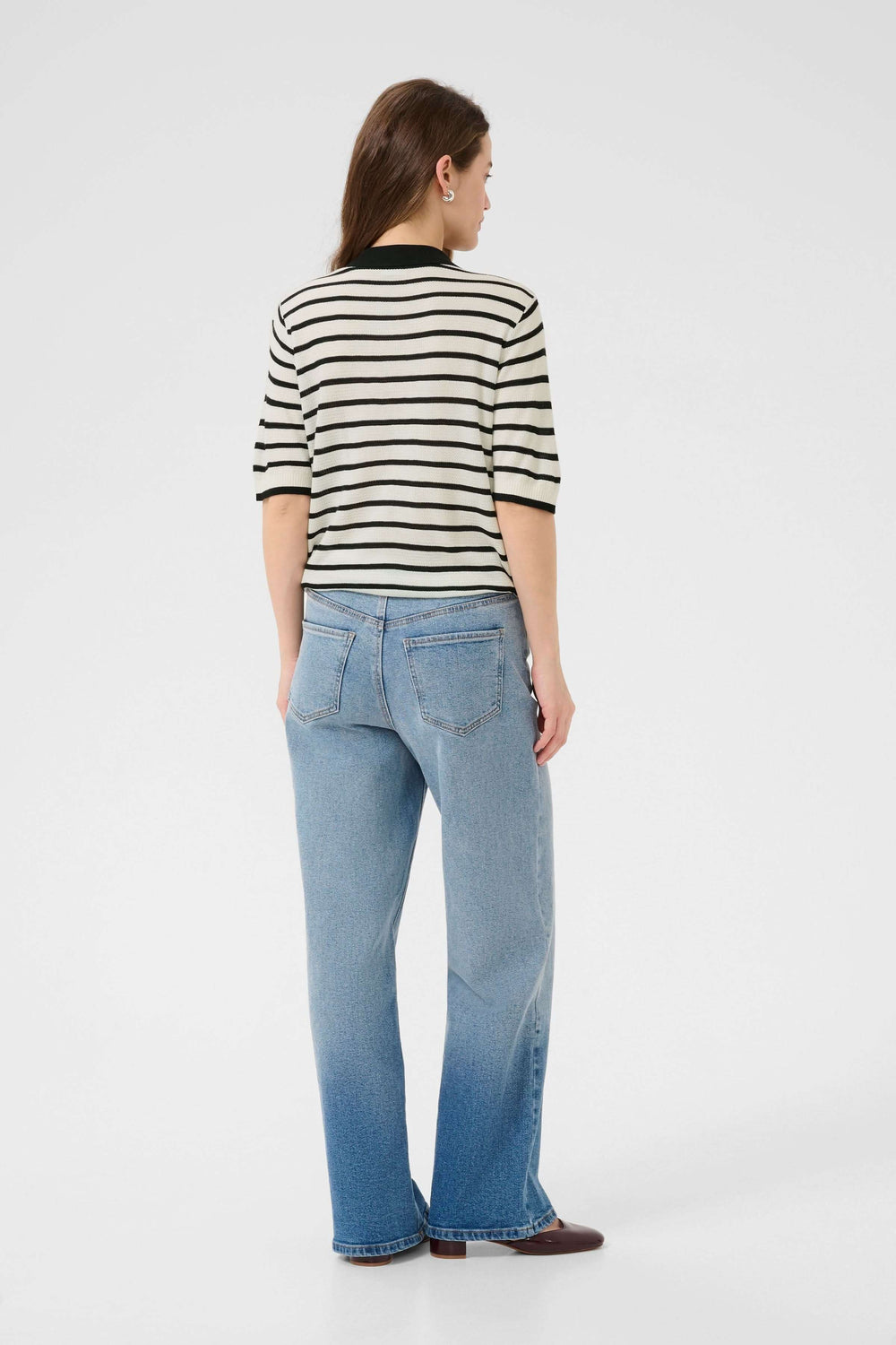 Femme de dos portant un polo rayé rétro-chic avec jean, style moderne et féminin pour un look casual.