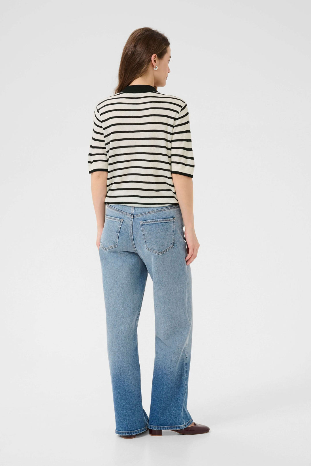 Femme de dos portant un polo rayé rétro-chic avec jean, style moderne et féminin pour un look casual.