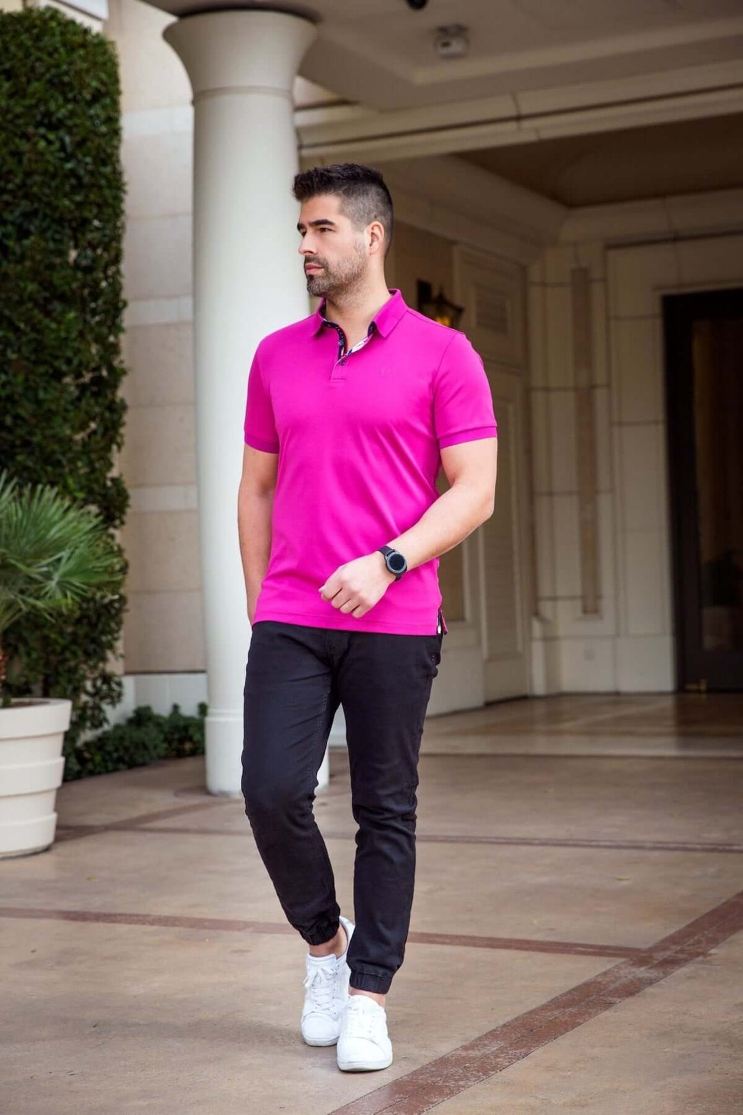 Homme portant un polo rose moderne avec col structuré et pantalon noir, déambulant dans un cadre élégant.