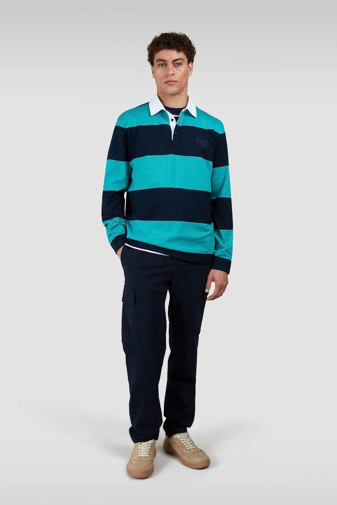 Homme portant un polo rugby à rayures turquoises et marine avec pantalon cargo, style urbain décontracté.